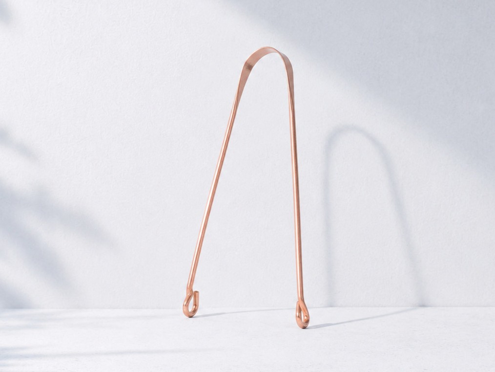 Close-up of a polished copper U-shape tongue scraper on a clean white surface
